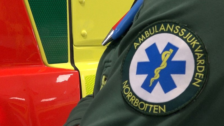 Bilden visar en person som står framför en ambulans med ambulanssjukvårds logotypen